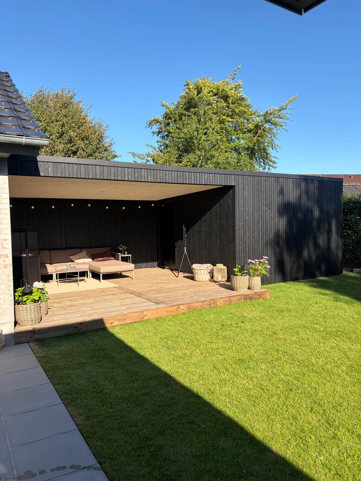 Færdig sort pavillon i baghaven med terrasse og græsplæne