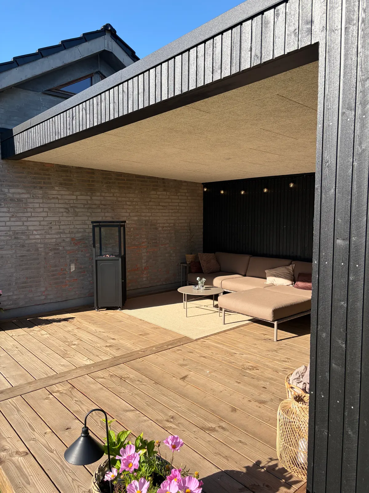 Sort beklædt pavillon med åben front og terrasse i en have